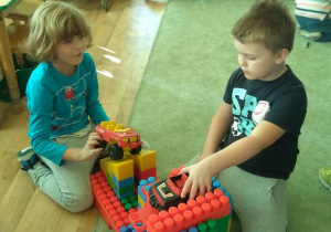 Chłopcy bawią się samochodami przy swojej budowli z klocków.